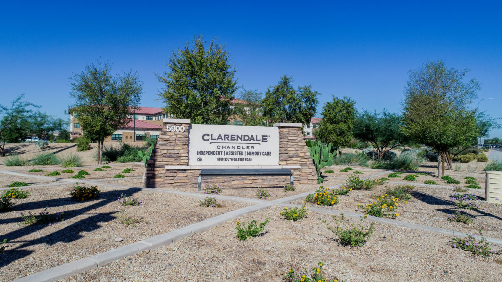 view of sign in front of building with flowers and trees around it