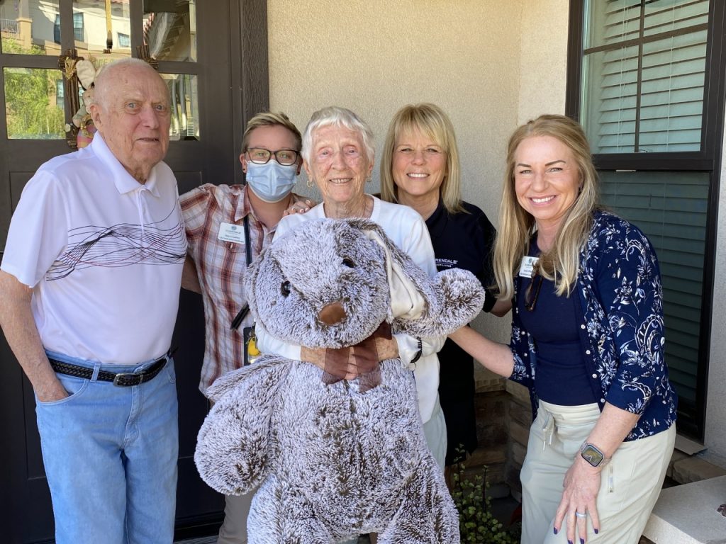 Elderly couple and Clarendale staff posing in a group on Easter with elderly woman holding oversized stuffed bunny rabbit prize.