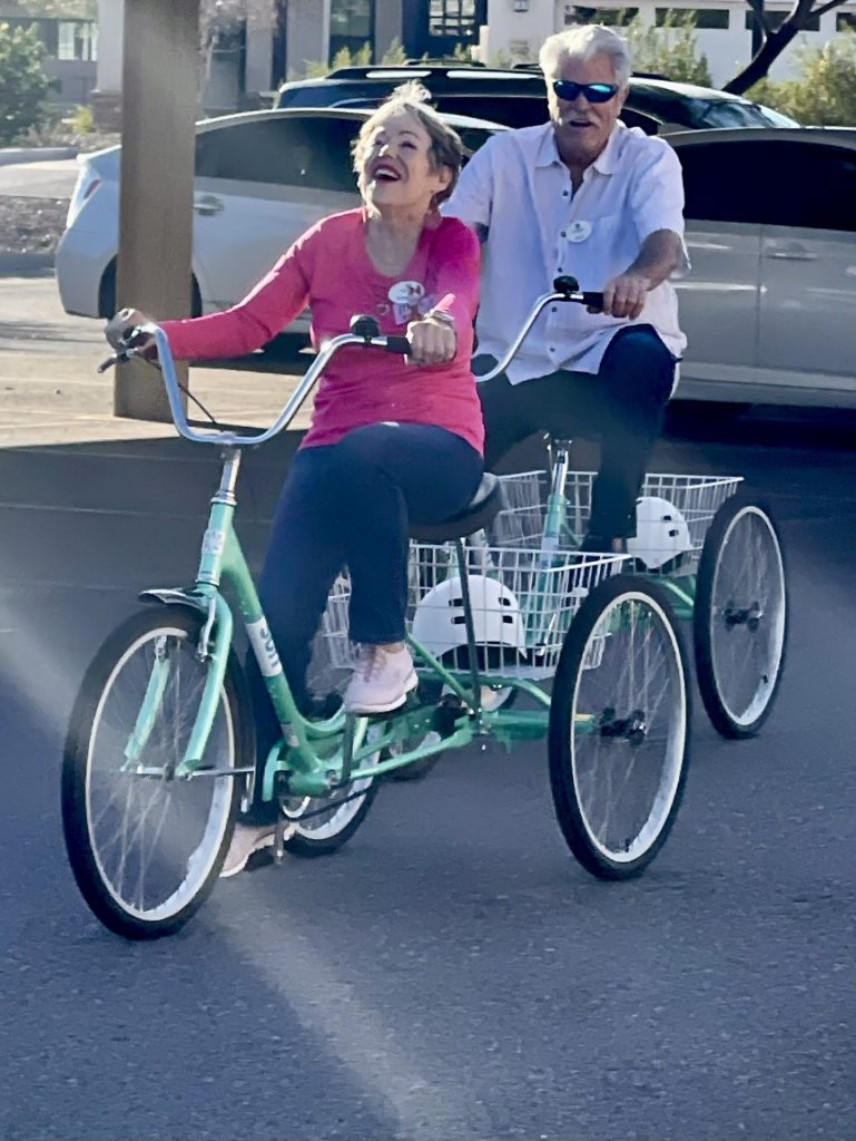 Elderly couple ride a tandem bike together, laughing.