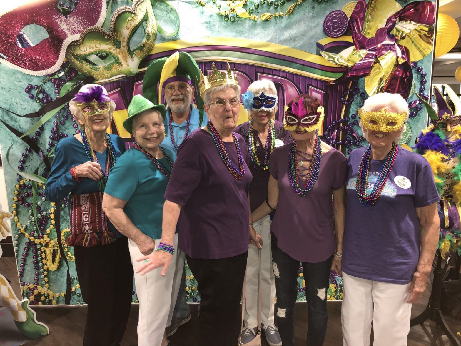 Senior residents pose in a group during Mardi Gras themed party, wearing Mardi Gras themed props.