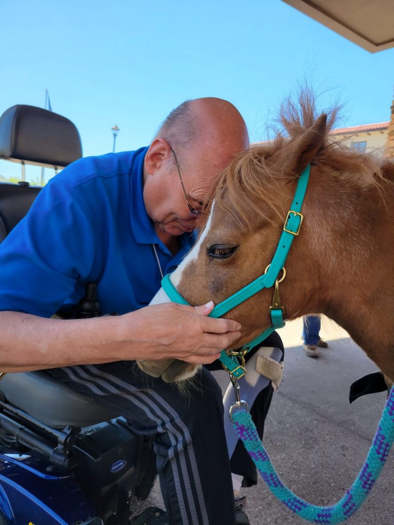 Man in wheel chair rests forehead on therapy horse's head in a moment of bonding.