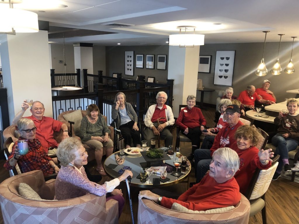 Large group of seniors sit around a community area, drinking wine and socializing