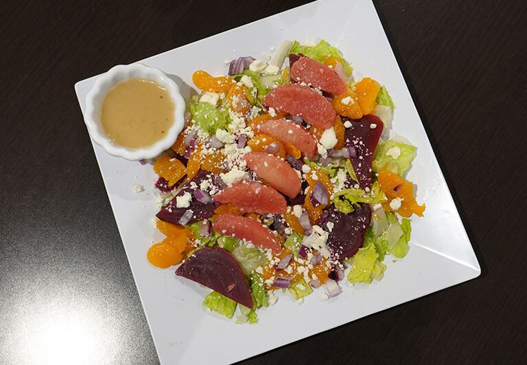 colorful-fresh-salad-dining6 Fresh salad with beets, grapefruit, oranges, and crumbled cheese on a white plate.
