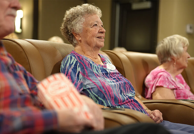 Elderly residents enjoying a movie screening in a community lounge area.