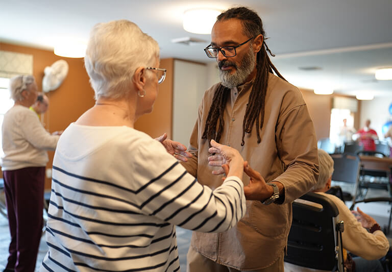 Elderly woman and instructor participate in a dance activity in a community room.