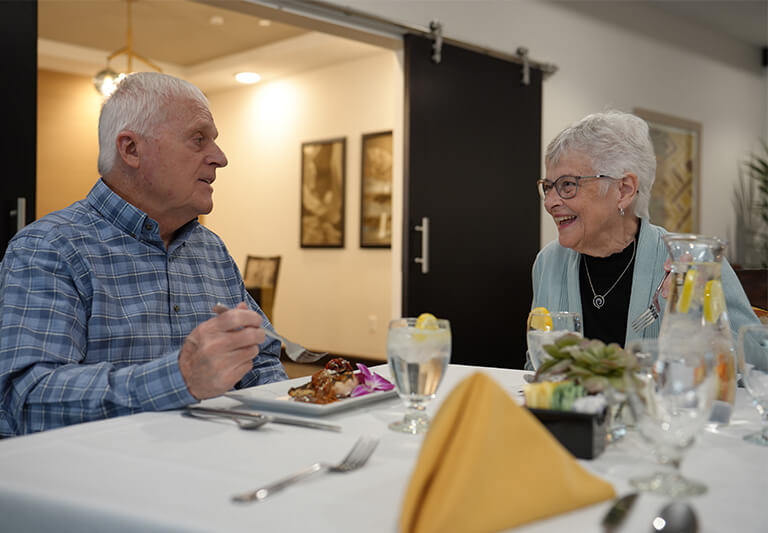 Elderly couple enjoying a meal at a dining area in a senior living community.