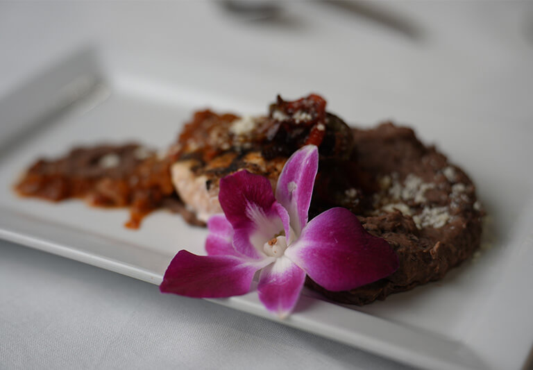 Gourmet meal with a pink orchid garnish served on a white plate.