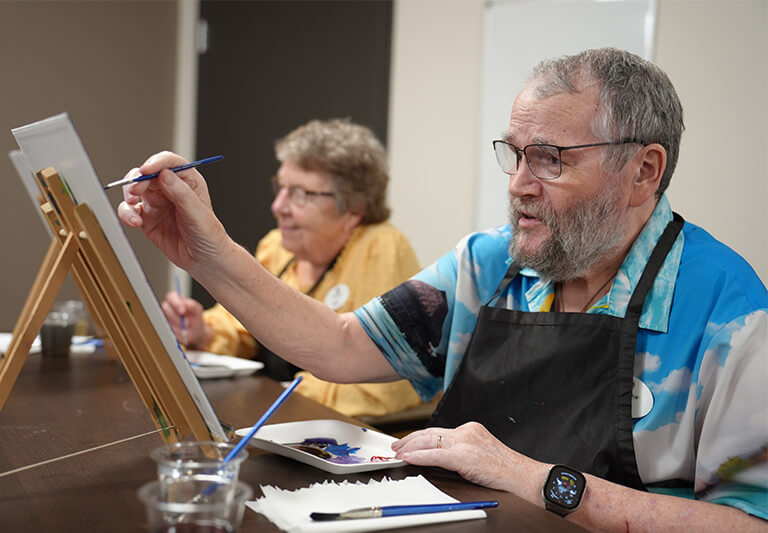 Two older adults engaged in a painting at a senior living community.