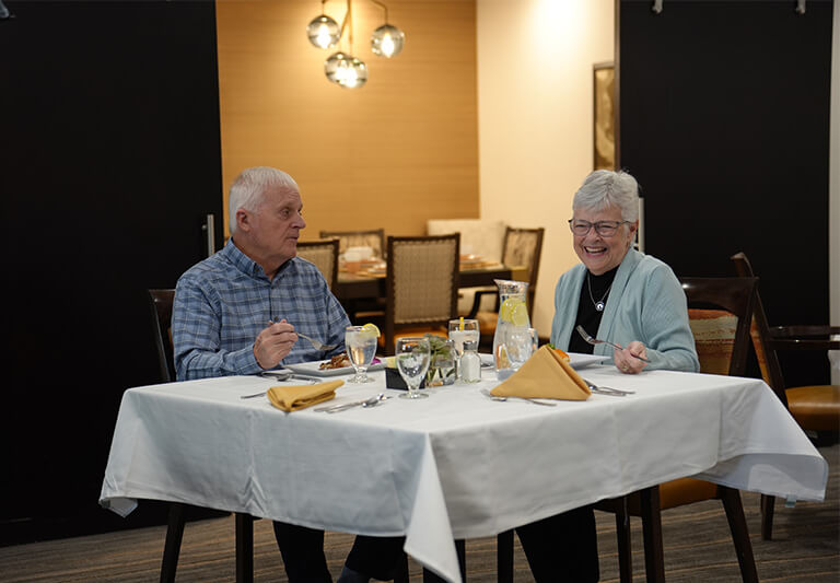 Two seniors enjoying a meal in a community dining area with modern decor.