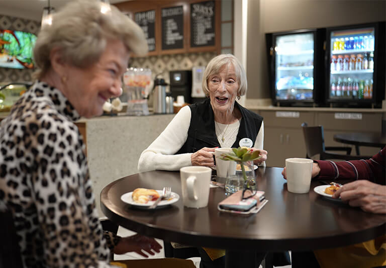 Three seniors enjoying coffee and snacks at a cafe in a community setting.